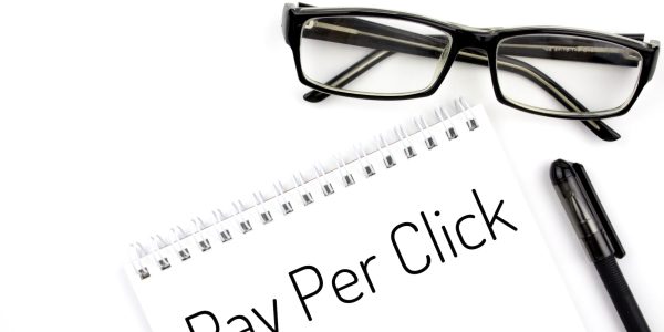 Reading glasses and notebook with word Pay Per Click on a white background